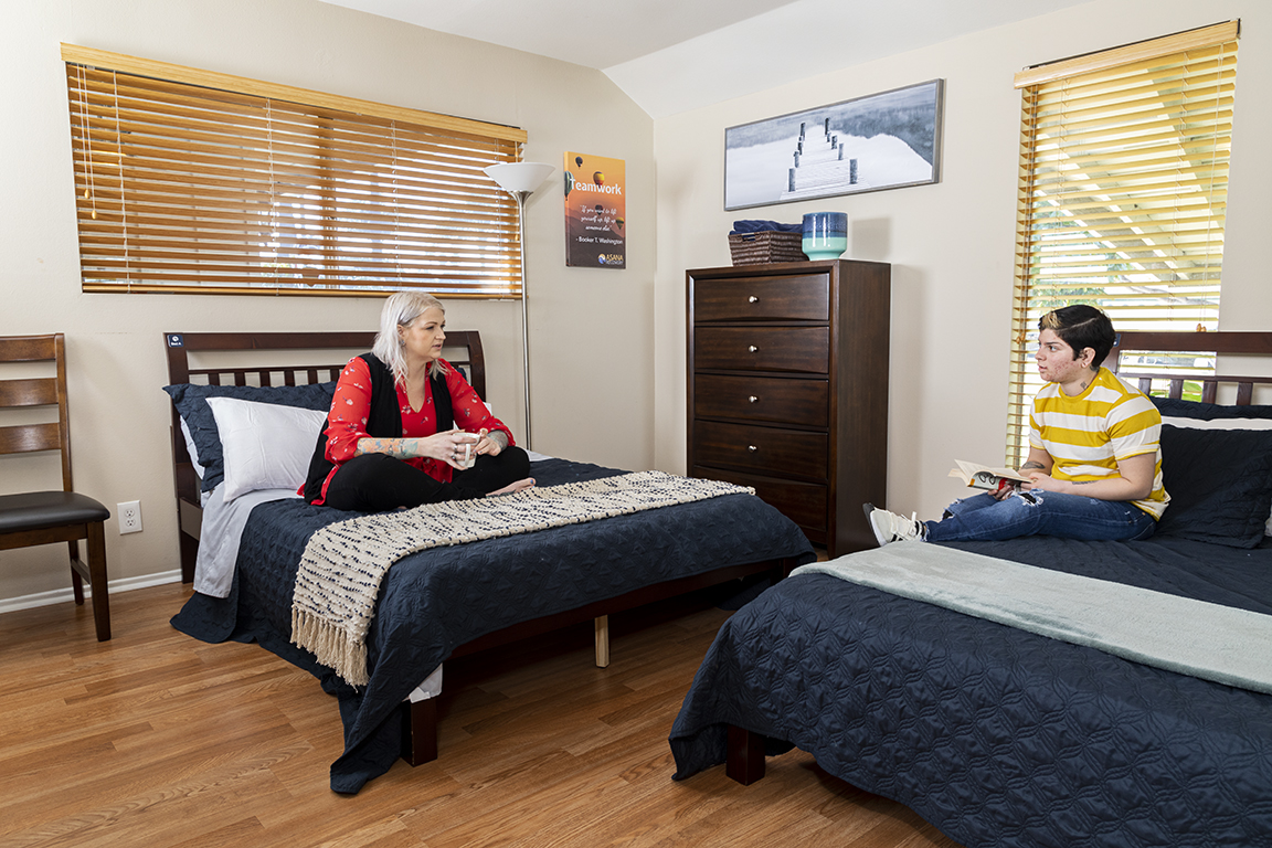Rehab bedroom with two beds, wooden furniture, and natural light.