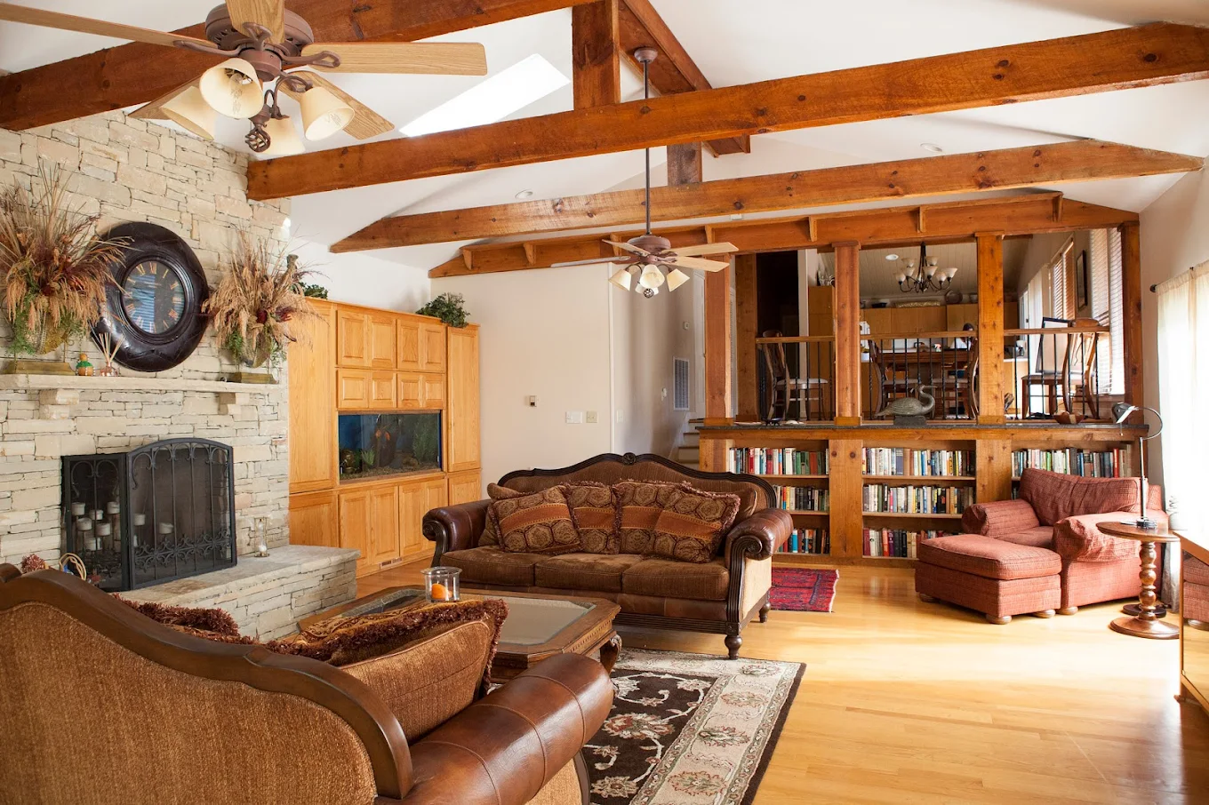 Warm-toned living room with wooden beams, fireplace, plush seating, and bookshelves