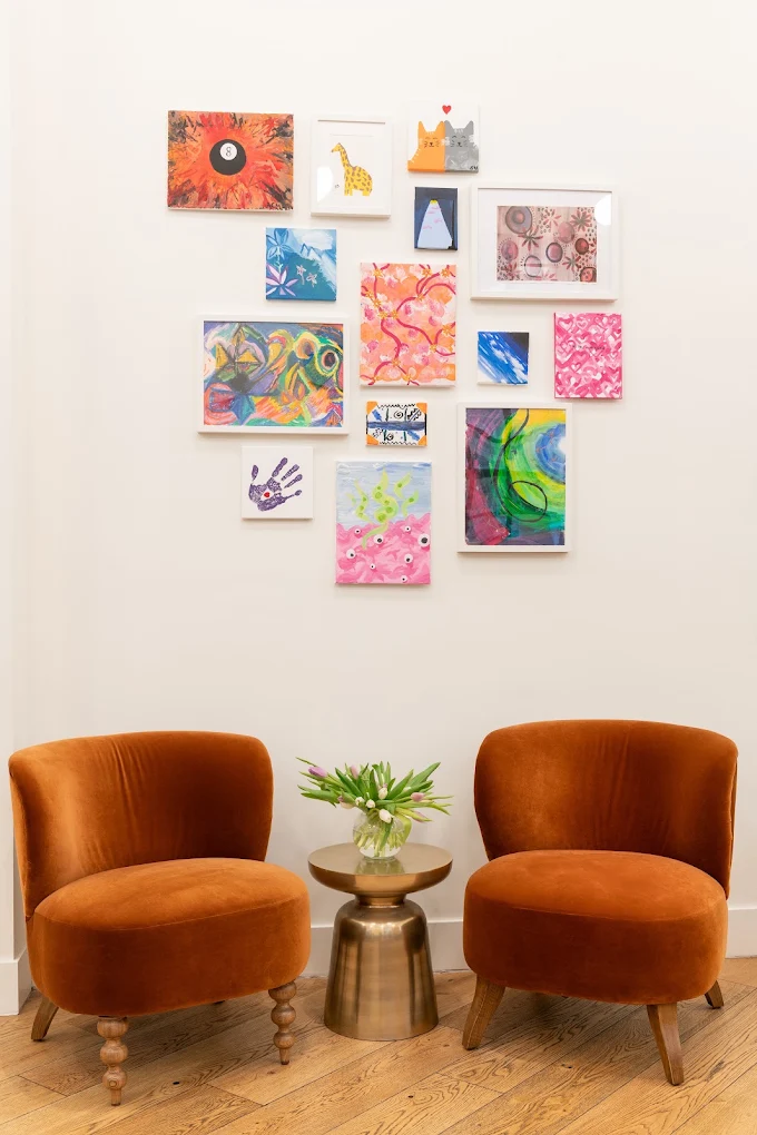 Two orange chairs beneath a colorful gallery wall