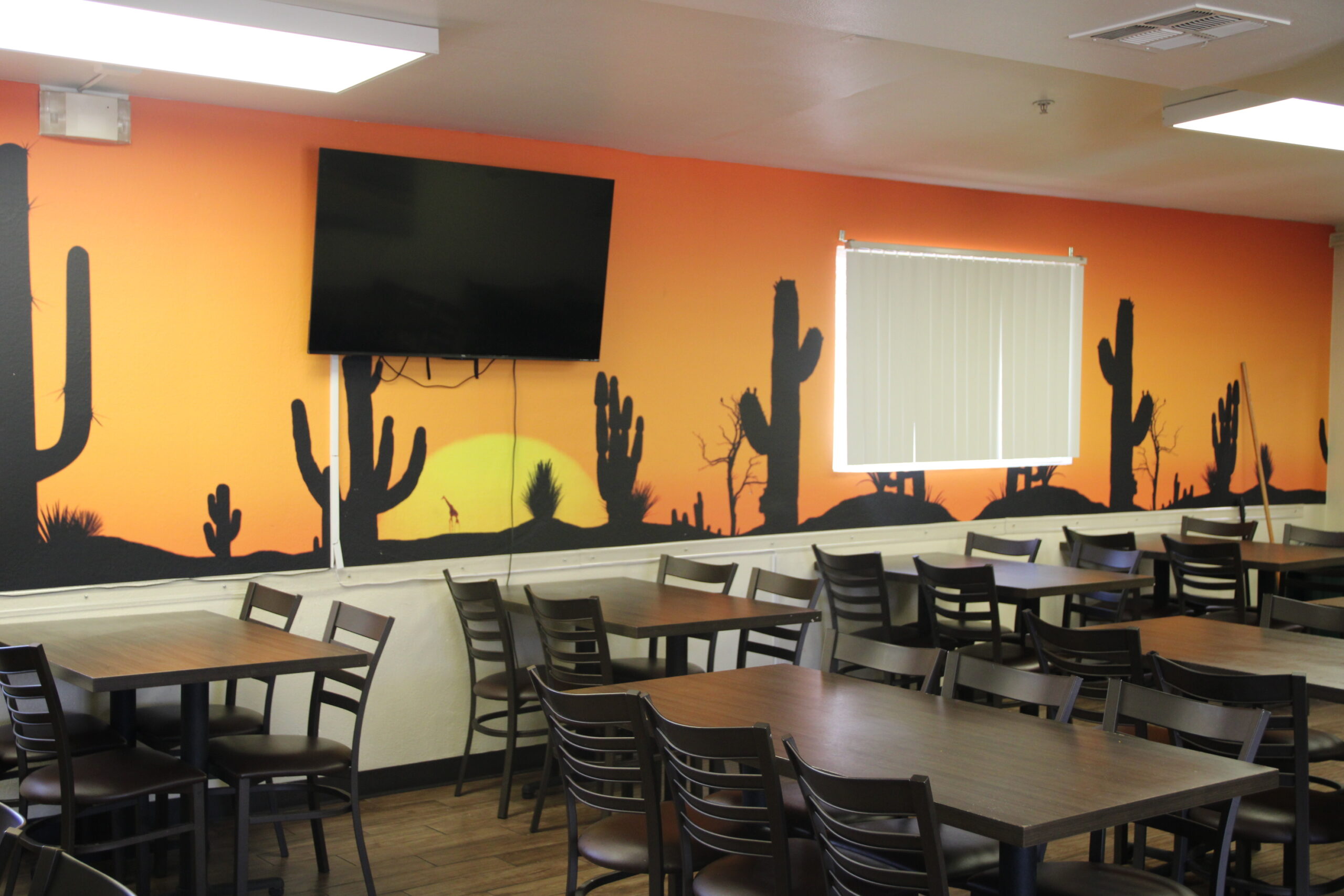 Dining area with sunset desert mural, flat-screen TV, and multiple tables with chairs