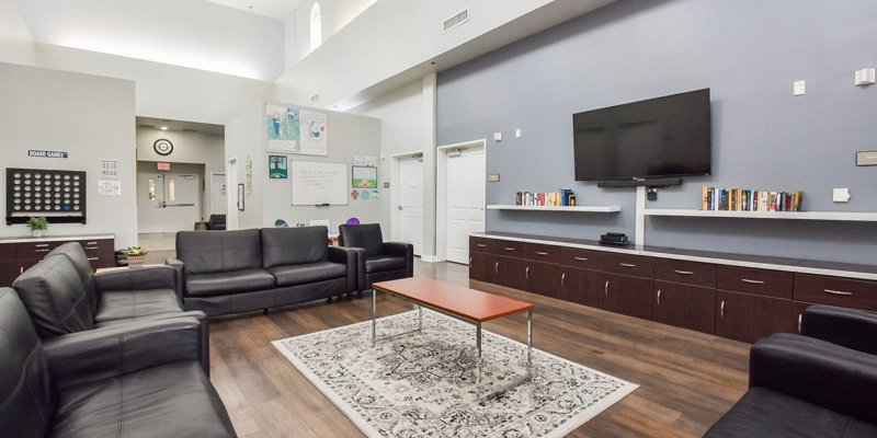  A spacious, well-lit common room with comfortable leather seating, a large TV, bookshelves, and a relaxing atmosphere perfect for group activities.