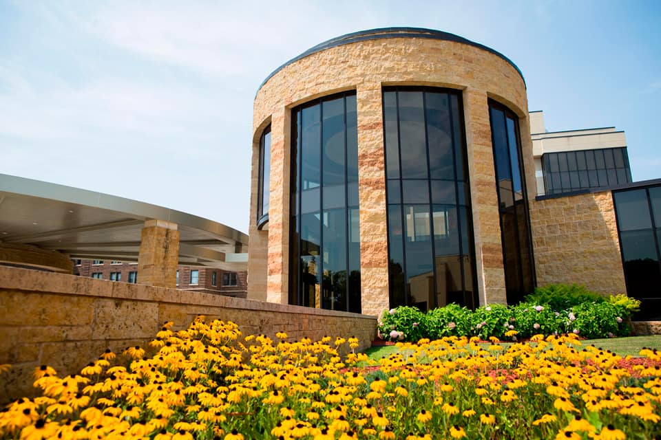 Stone facility exterior with tall windows and flower garden