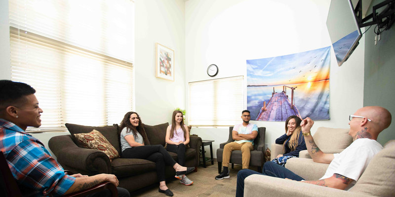 A group of people sitting comfortably in a bright room, engaging in a friendly conversation, fostering a relaxed and supportive environment for sharing.