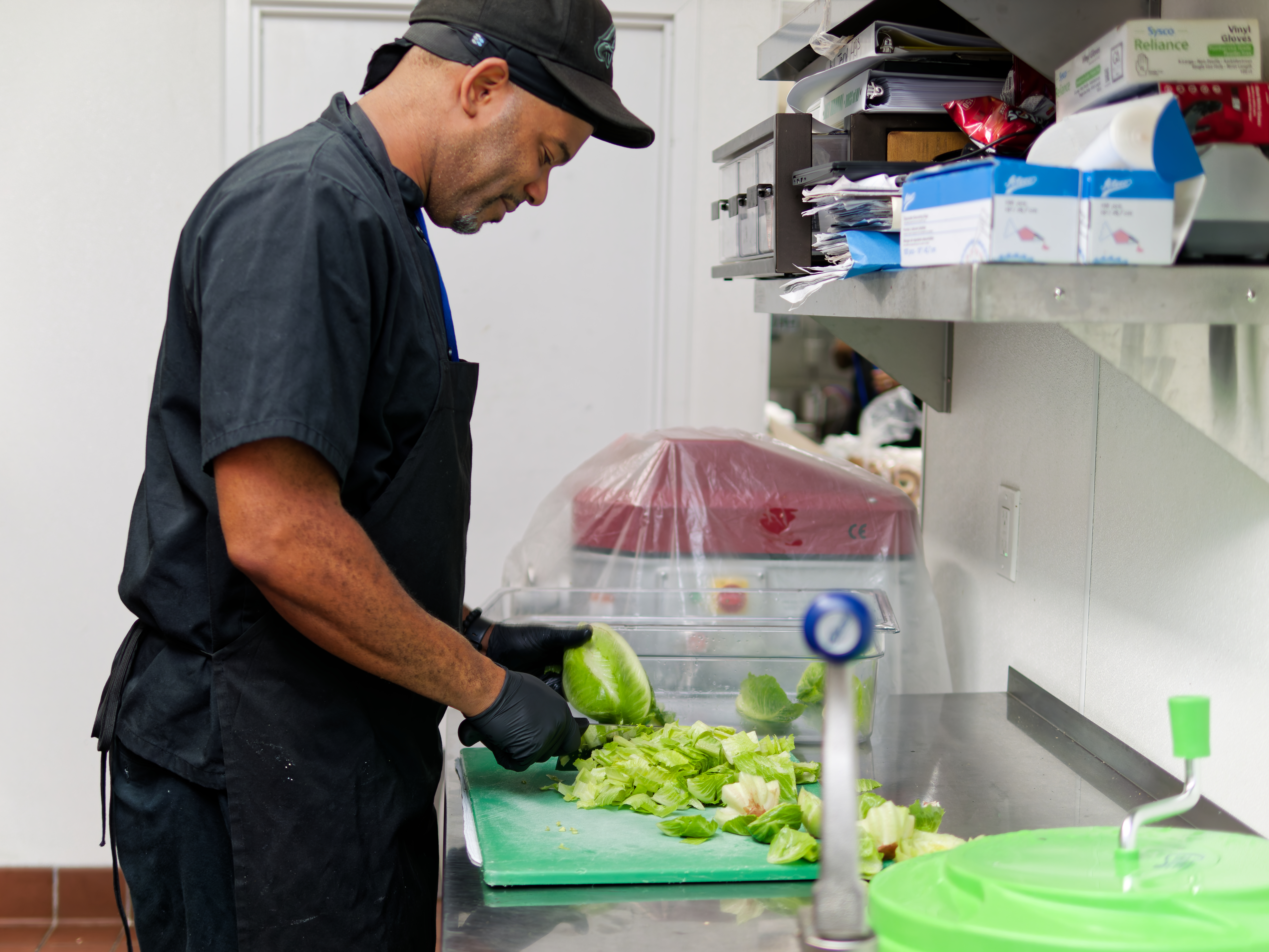 Chef chopping lettuce on a prep table in facility kitchen.