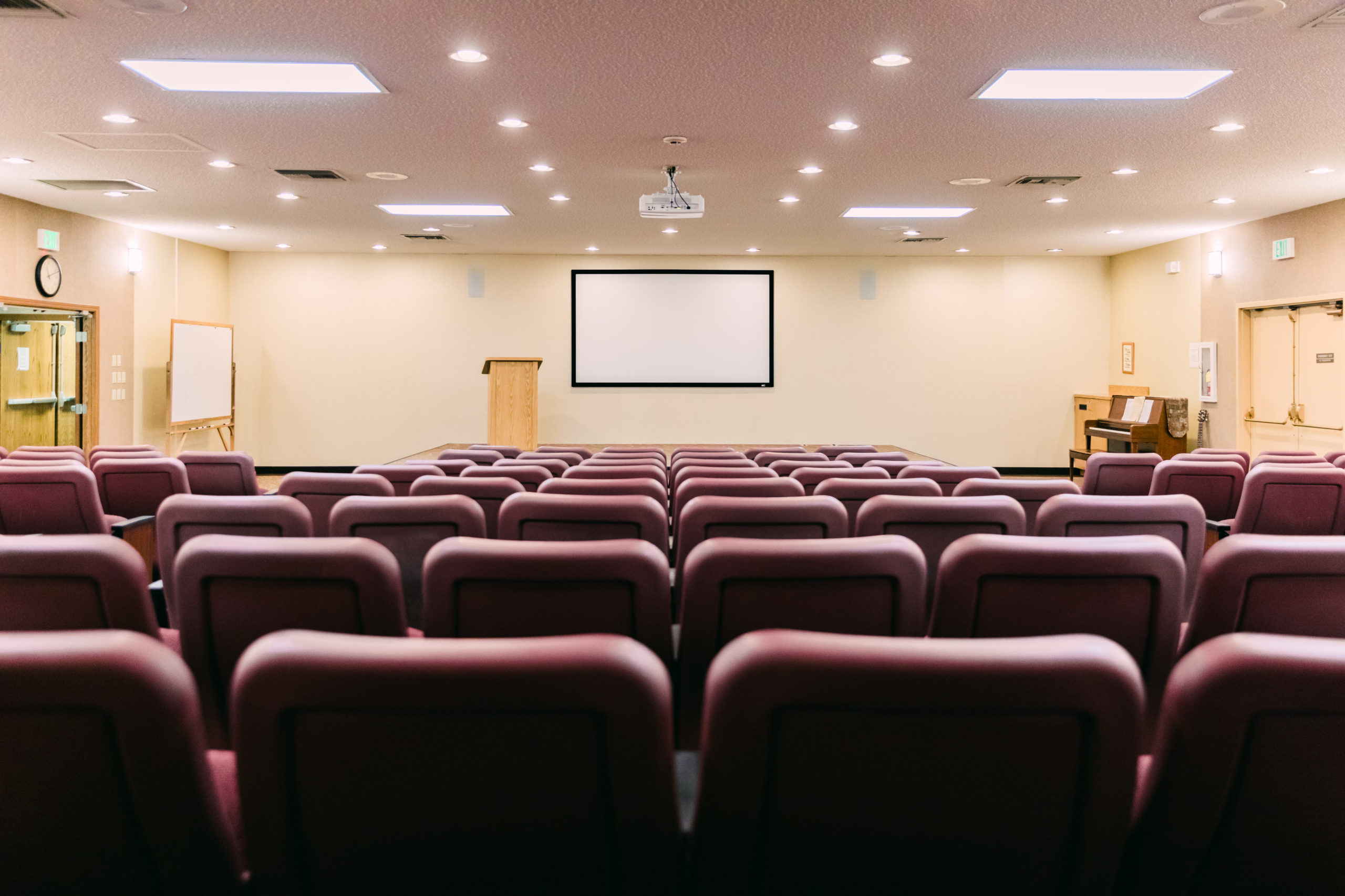 Rows of red chairs facing screen and podium
