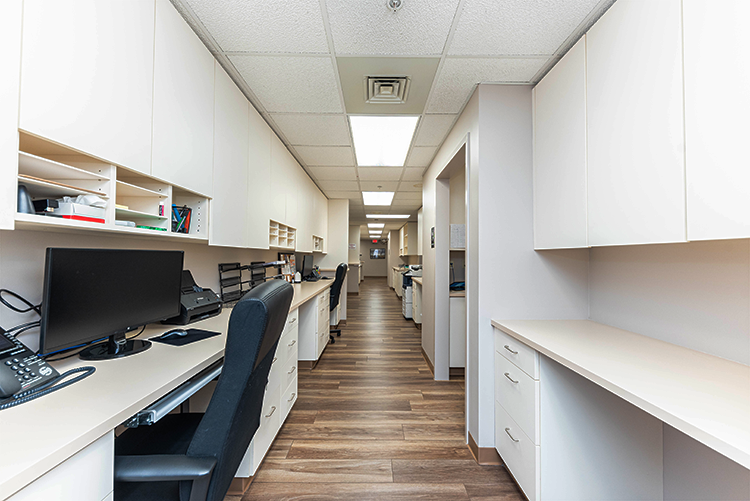 BrightView Health staff workstation with computer, telephone, white cabinets, counters, wood-look flooring, and a long clinical hallway