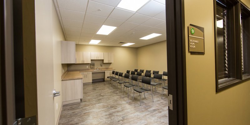 A bright and organized meeting room with comfortable chairs and a small kitchenette. The clean space is perfect for group sessions or workshops.