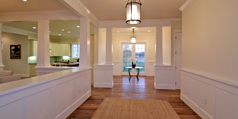 A bright, inviting hallway with warm wood flooring and elegant lighting leads to a cozy sitting area, creating a welcoming atmosphere.