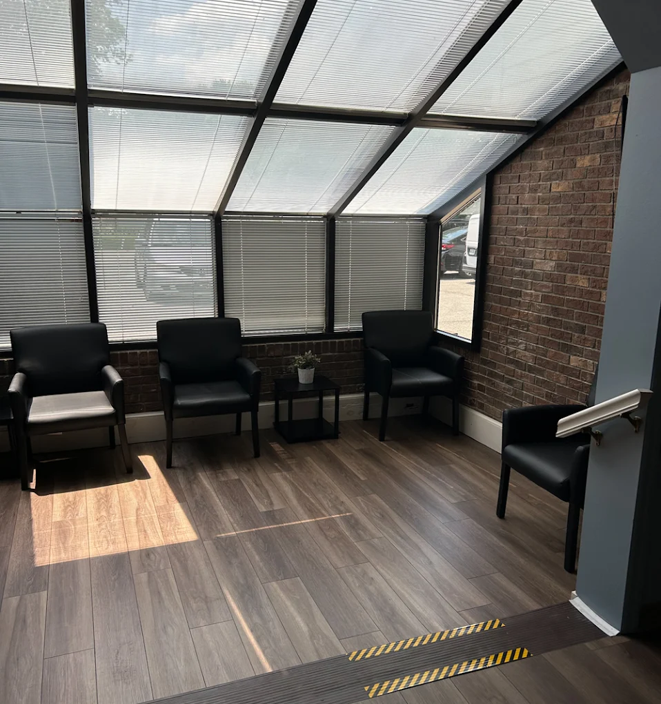 BrightView Health sunroom waiting area with black armchairs, brick walls, large windows with blinds, and wood-look flooring