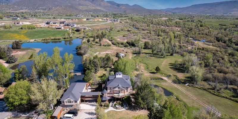  Aerial view of a serene countryside estate surrounded by lush greenery, lakes, and mountain views, offering a peaceful and expansive setting.