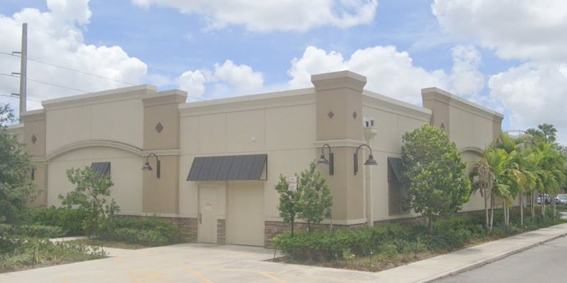  A light beige building with decorative trim, lush landscaping, and a clear sky backdrop.