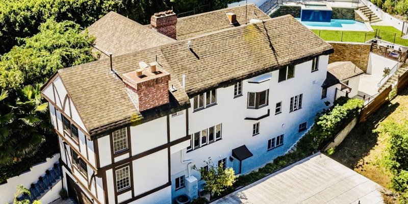 Charming multi-level home with Tudor-style accents, nestled among lush greenery, featuring a cozy rooftop and private backyard pool.