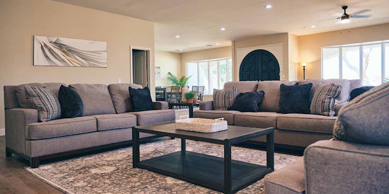 A cozy living room featuring comfortable gray sofas with plush pillows, a stylish coffee table, and warm lighting, creating a welcoming atmosphere.