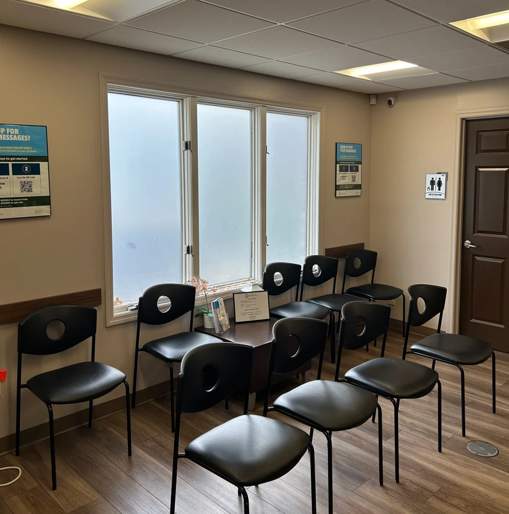 BrightView Health treatment room with rows of black chairs, frosted windows, small central table, restroom entrance, and wood-look flooring