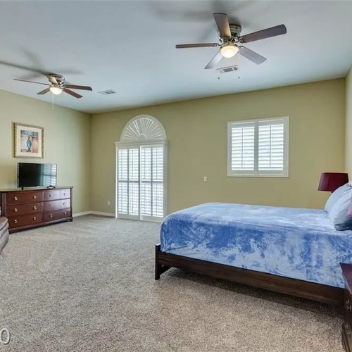 Spacious bedroom with bed, dresser, TV, and ceiling fans