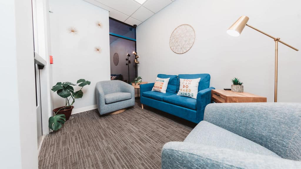 Therapist’s office with blue sofa, chairs, and gold floor lamp
