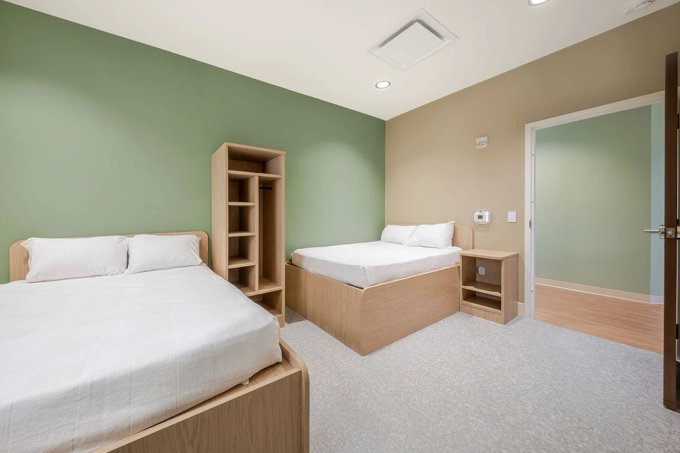 Shared residential bedroom with two beds, light wood furniture, and soft green walls