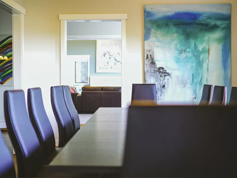 Dining area with long table, chairs, and large abstract wall art