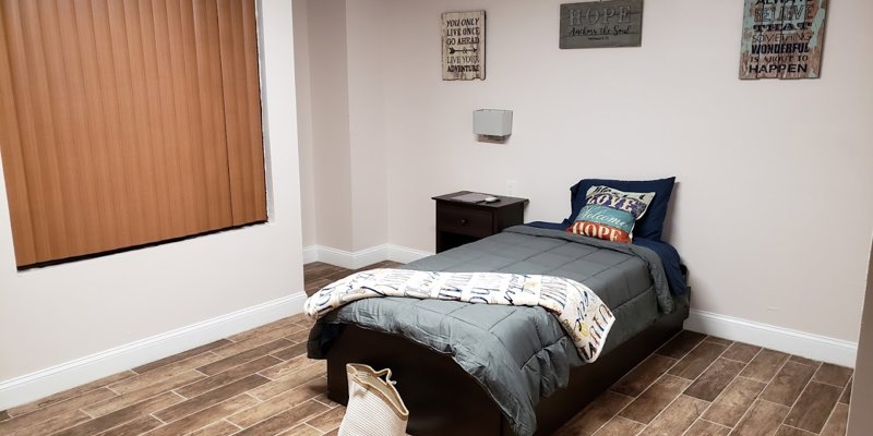 A cozy bedroom with a single bed, inspirational wall art, warm wood flooring, and soft lighting, creating a comforting and serene environment.