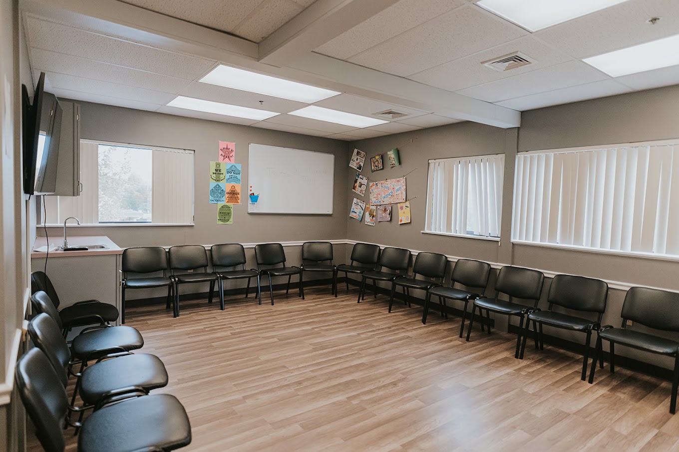 Group therapy room with black chairs in a circle, a TV and a board.