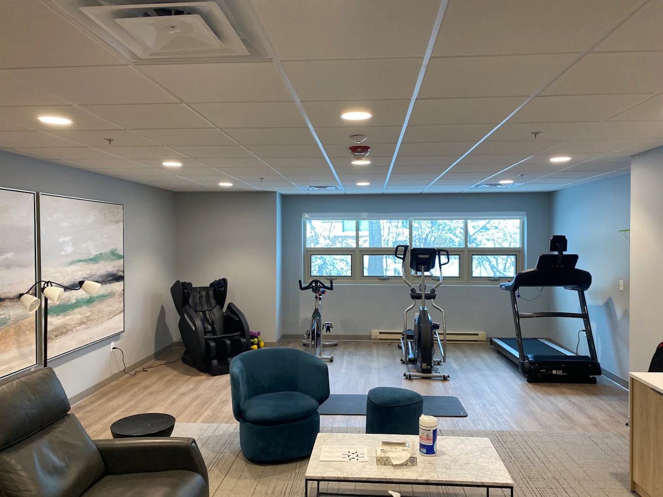 Fitness room with cardio equipment, seating, and large windows