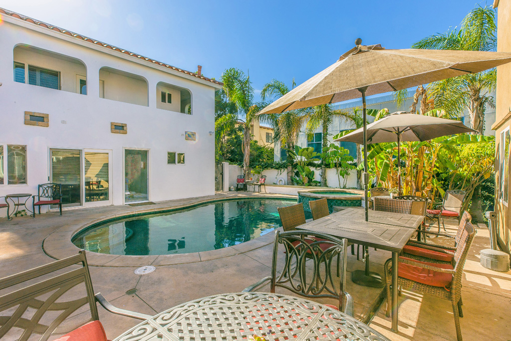 Backyard pool with patio tables, umbrellas, and palm trees
