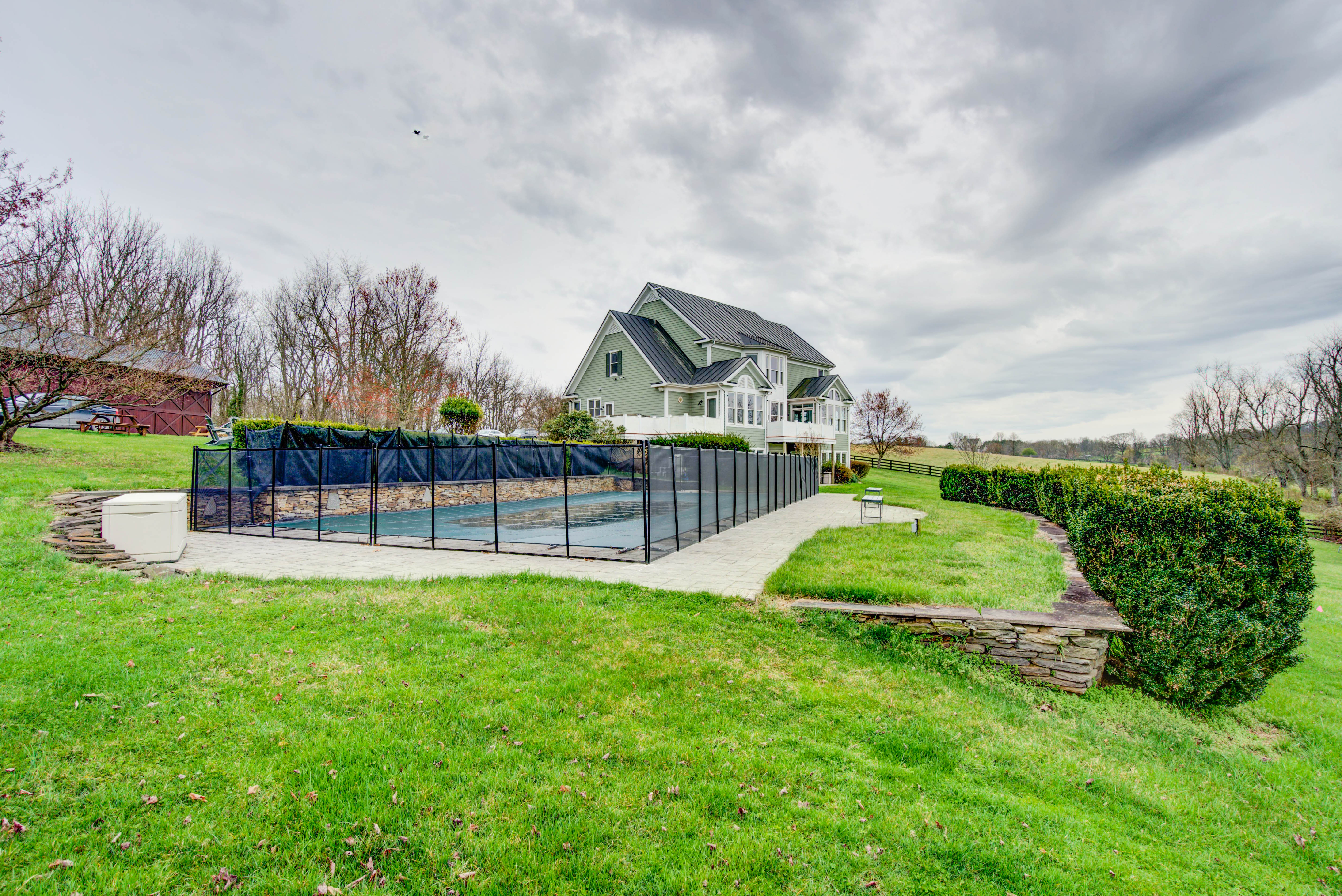Fenced outdoor pool beside a large house and green lawn