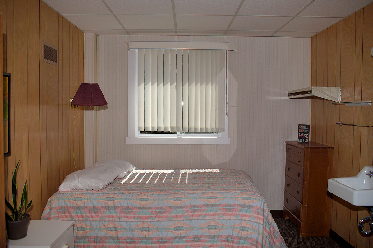 Simple residential bedroom with bed, dresser, and natural light