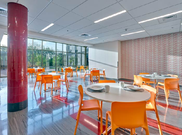 Dining lounge with tables and chairs near large windows.
