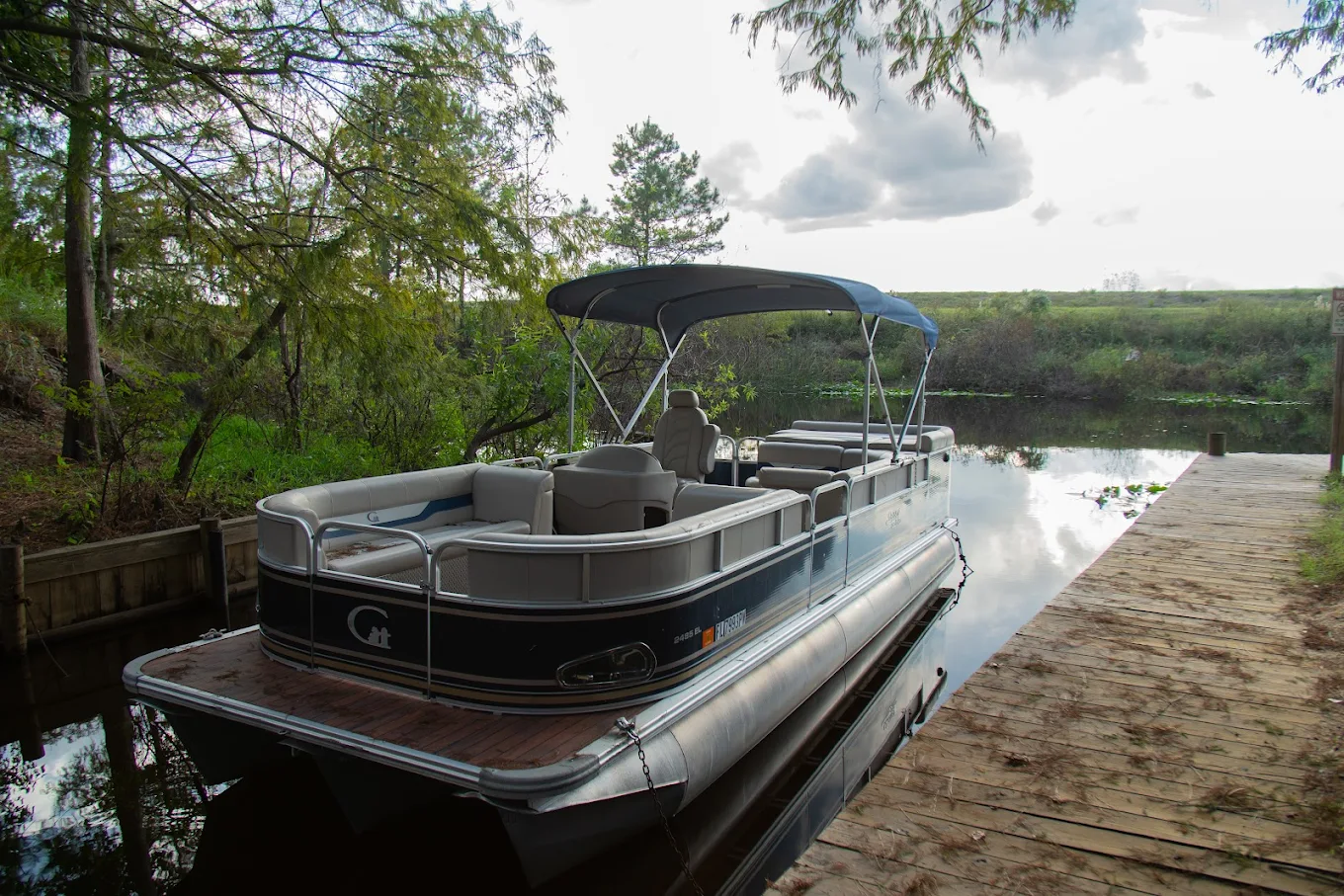 Pontoon boat docked along a wooded waterway