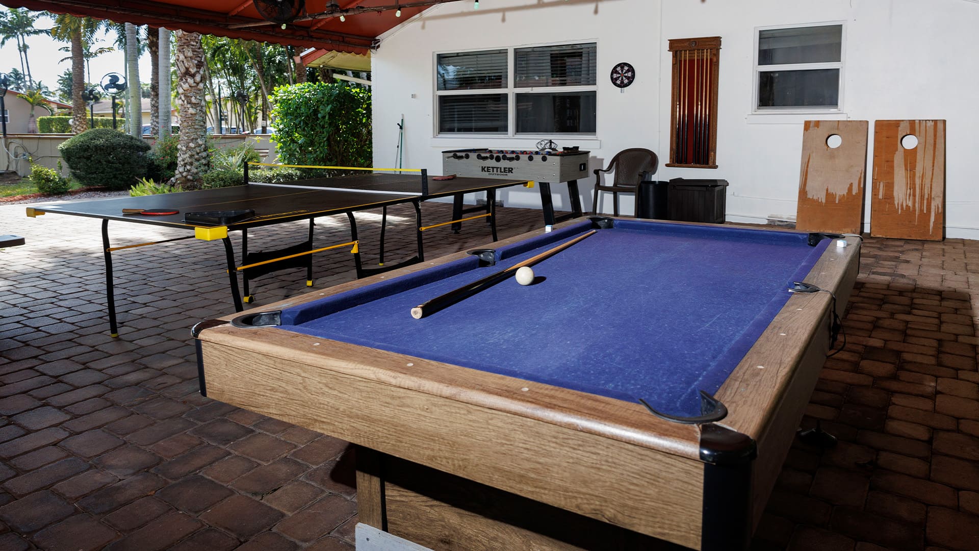 Covered outdoor game area with pool table, ping-pong, and seating.