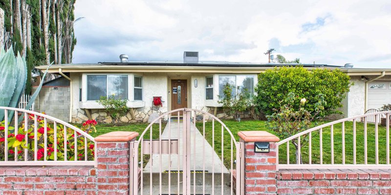  Charming single-story home with a gated entry, surrounded by lush greenery and vibrant flowers, offering a welcoming and cozy atmosphere.