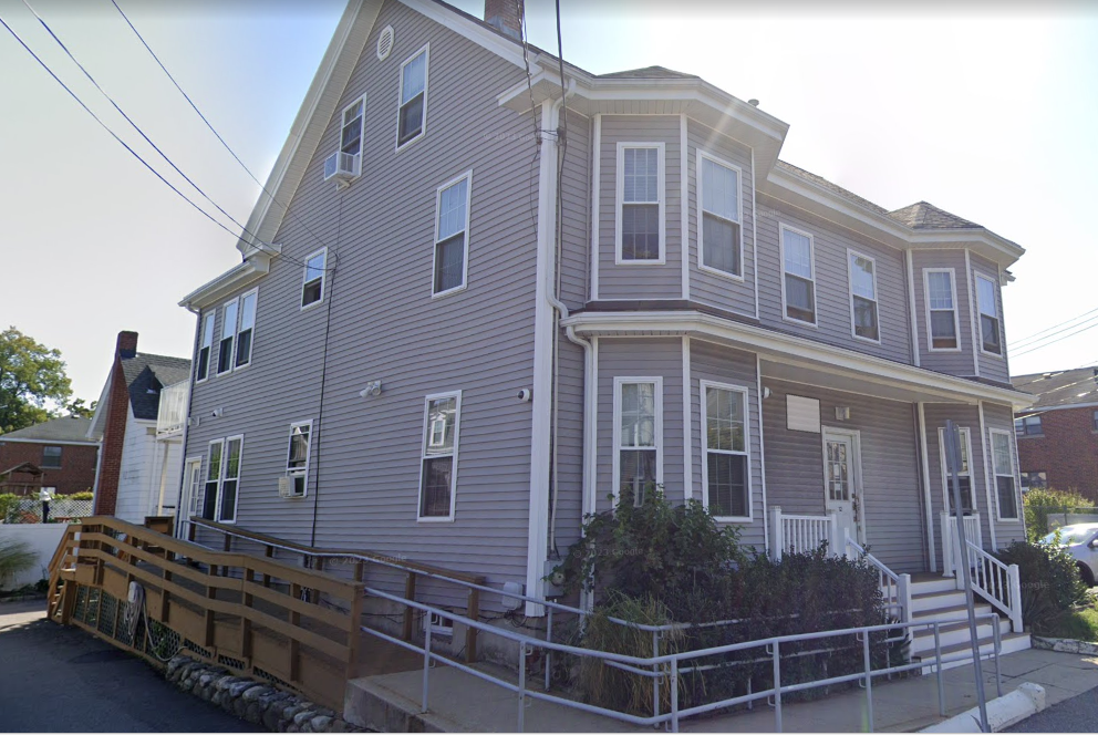 Side angle of gray recovery home with wooden ramp and porch