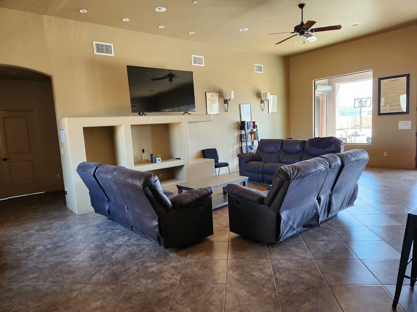 Spacious communal lounge with sofas, recliners, television, and tiled flooring