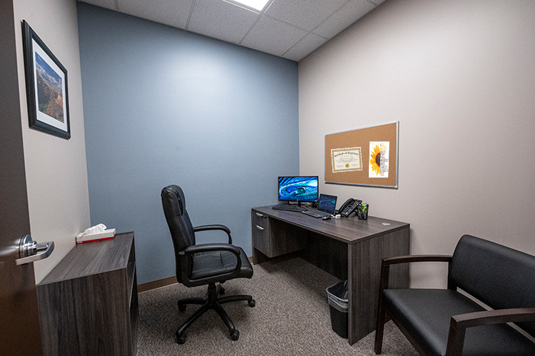 Private clinical office with desk, computer, office chair, guest seating, bulletin board, and blue accent wall