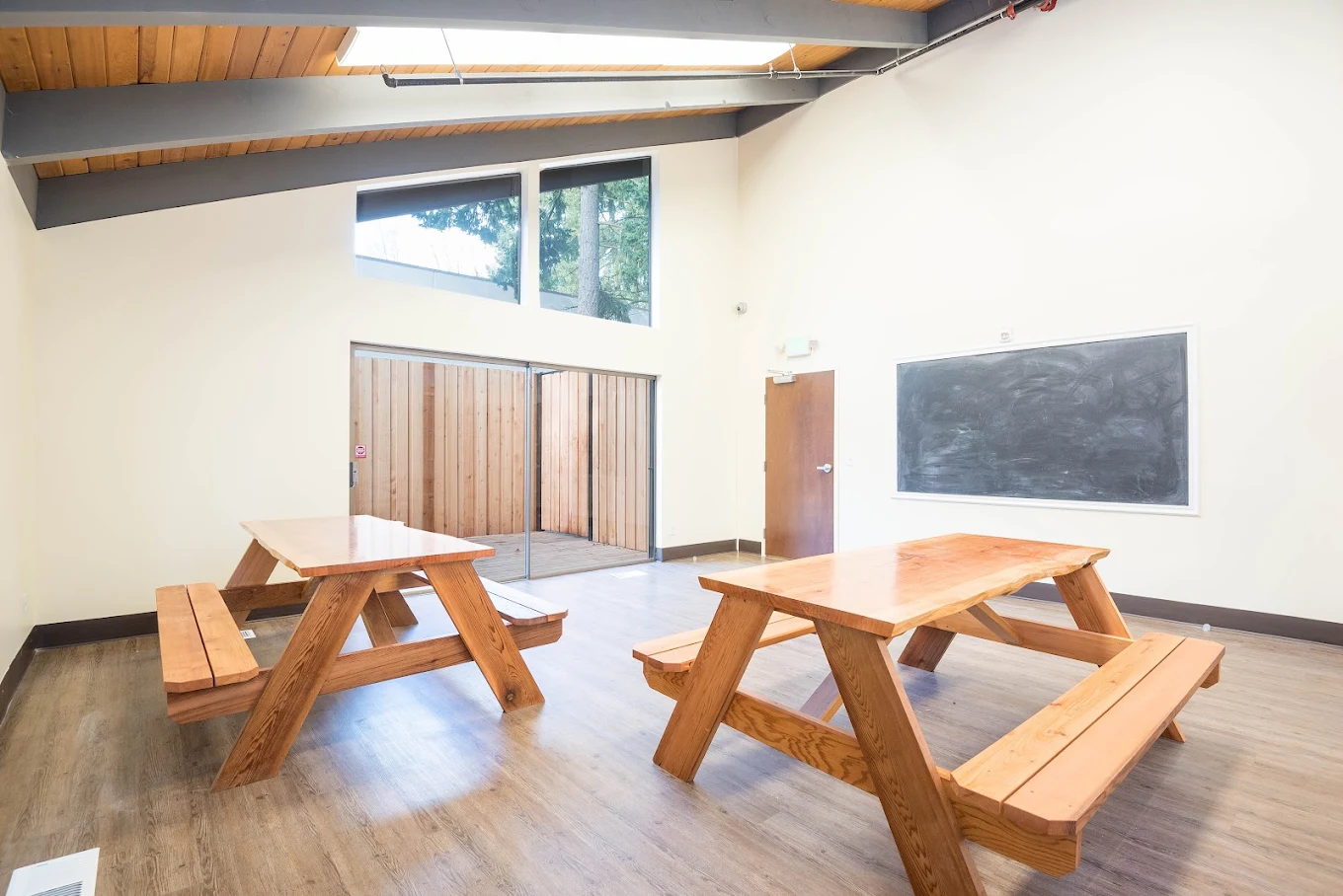 Bright activity room with wood picnic tables, chalkboard, and natural light from large windows
