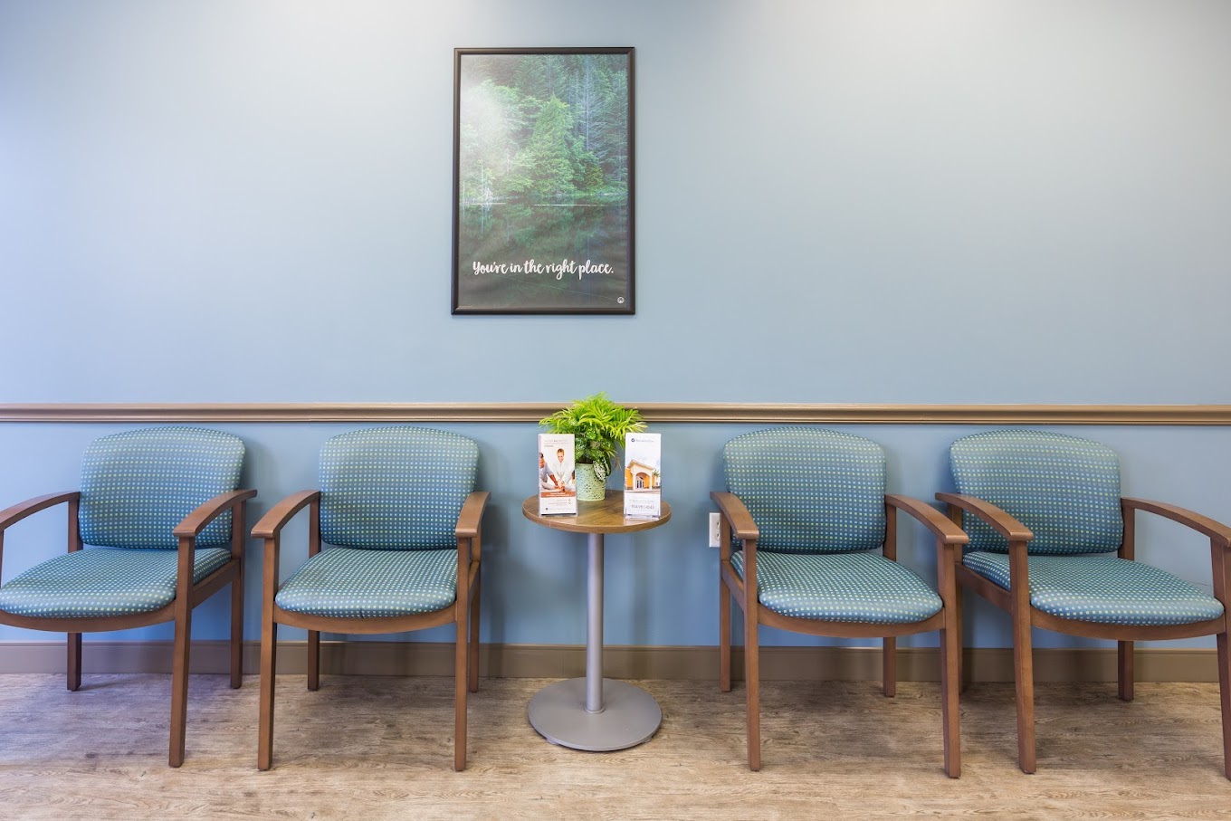 Waiting area with blue chairs, a round table, and a framed wall poster.