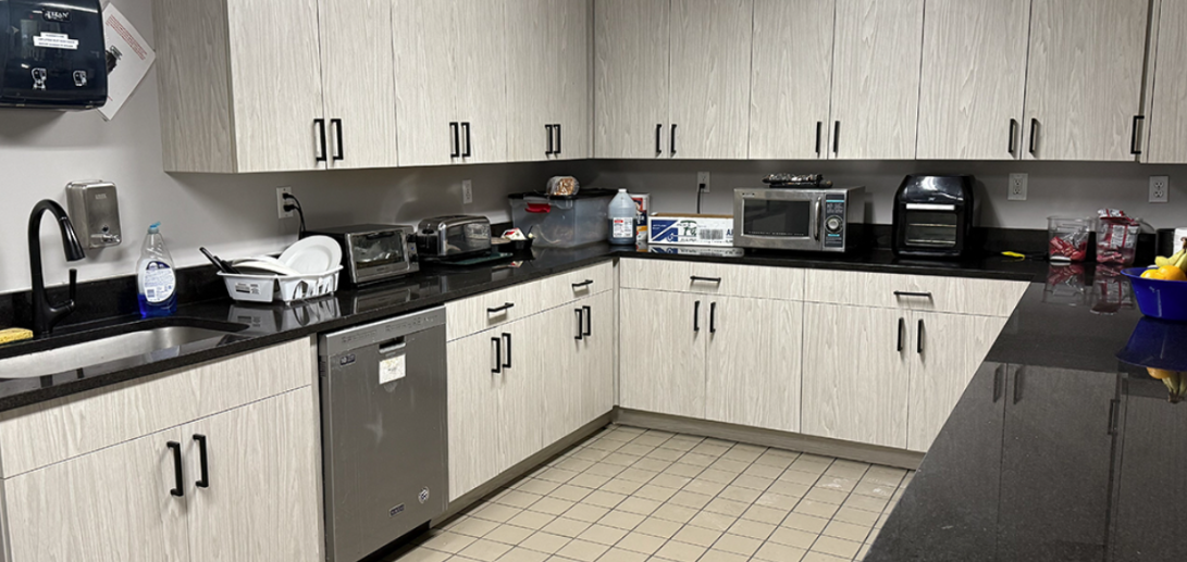 Modern communal kitchen with light wood cabinets, black countertops, and appliances