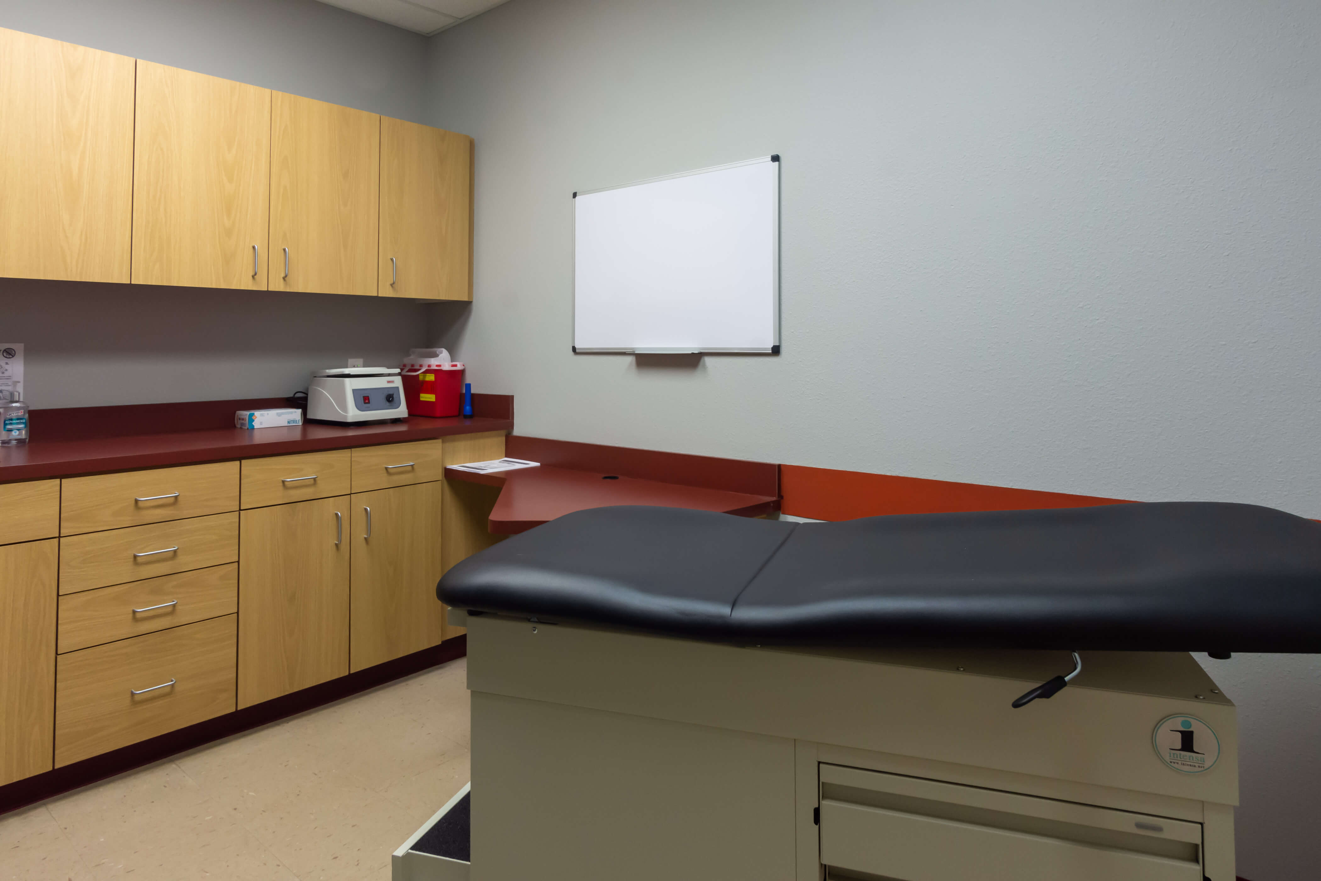 A medical exam room with a black examination table and wooden cabinets.