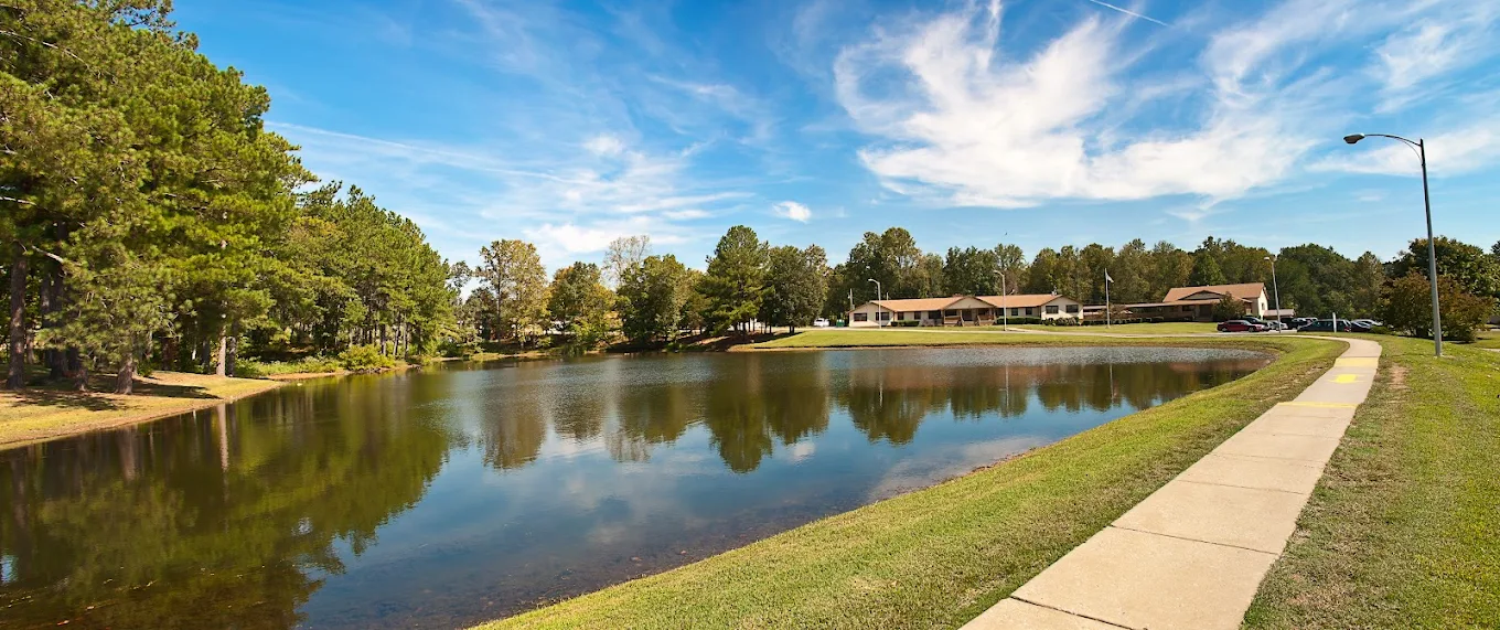 Lake reflecting trees and facility buildings under a blue sky