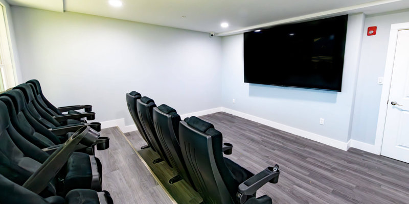 Comfortable theater room with plush seating and a large wall-mounted screen, offering a relaxing space for group viewings and presentations.