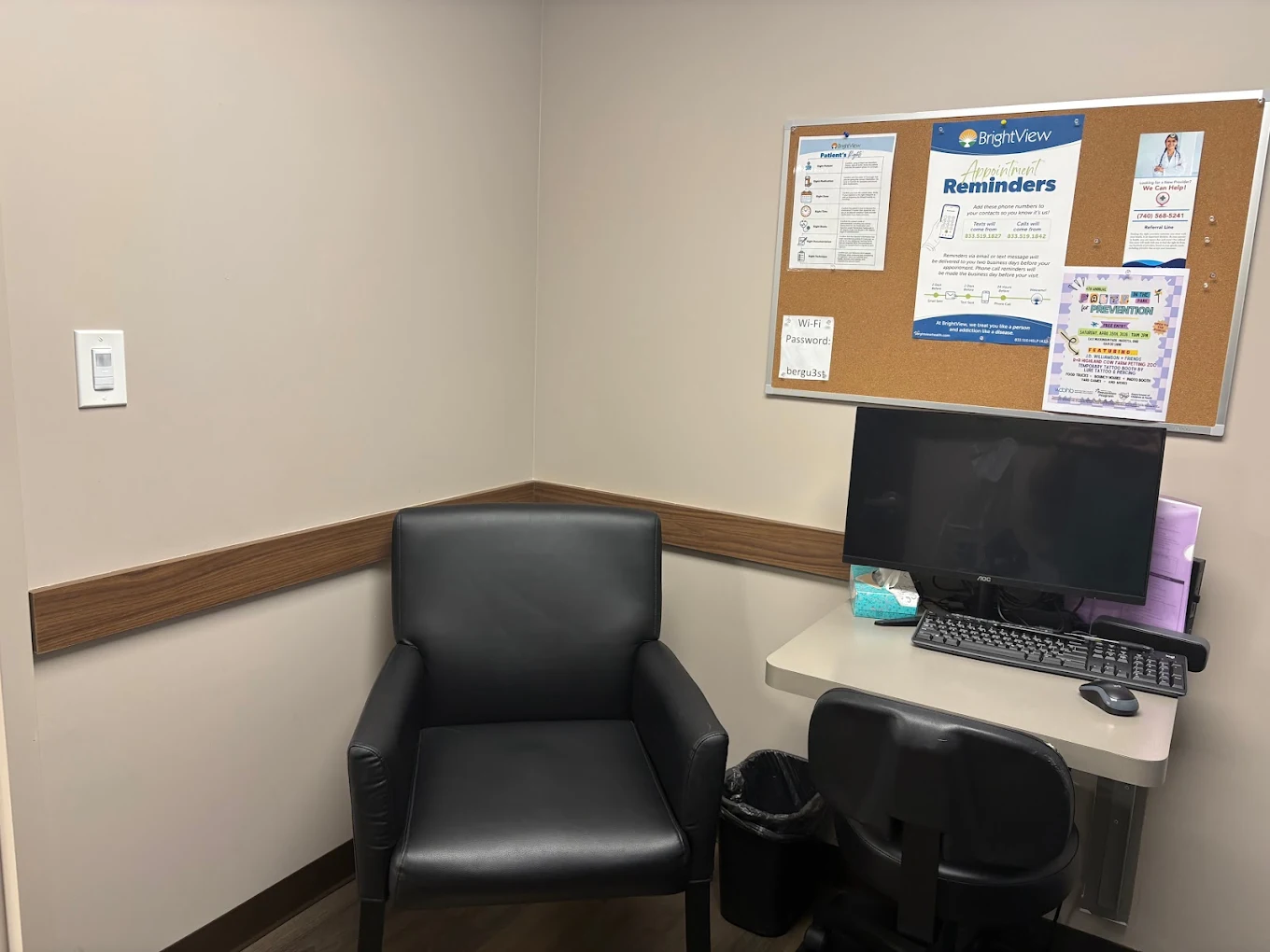Small consultation room at BrightView Health Marietta with black patient chair, computer workstation, bulletin board with appointment information, and wood wall trim