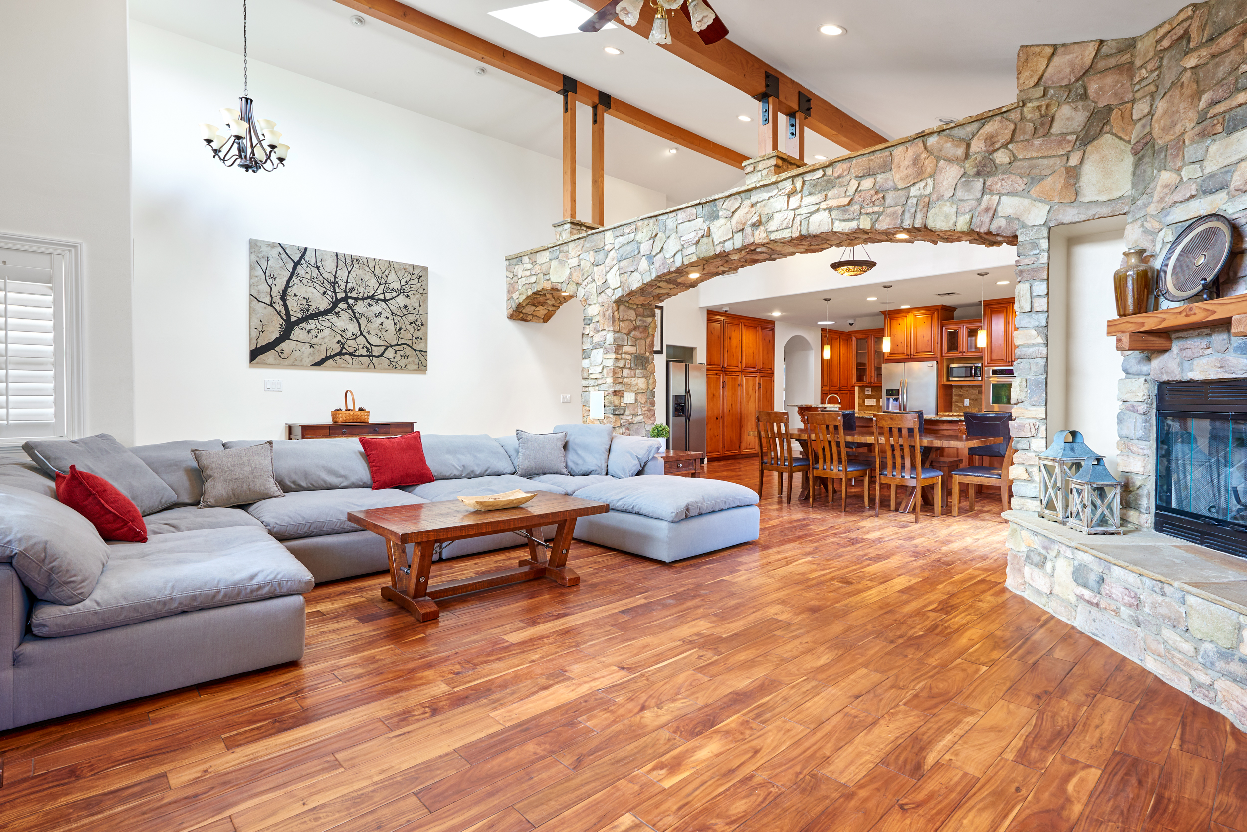 Living room with gray sectional and open stone arch to kitchen