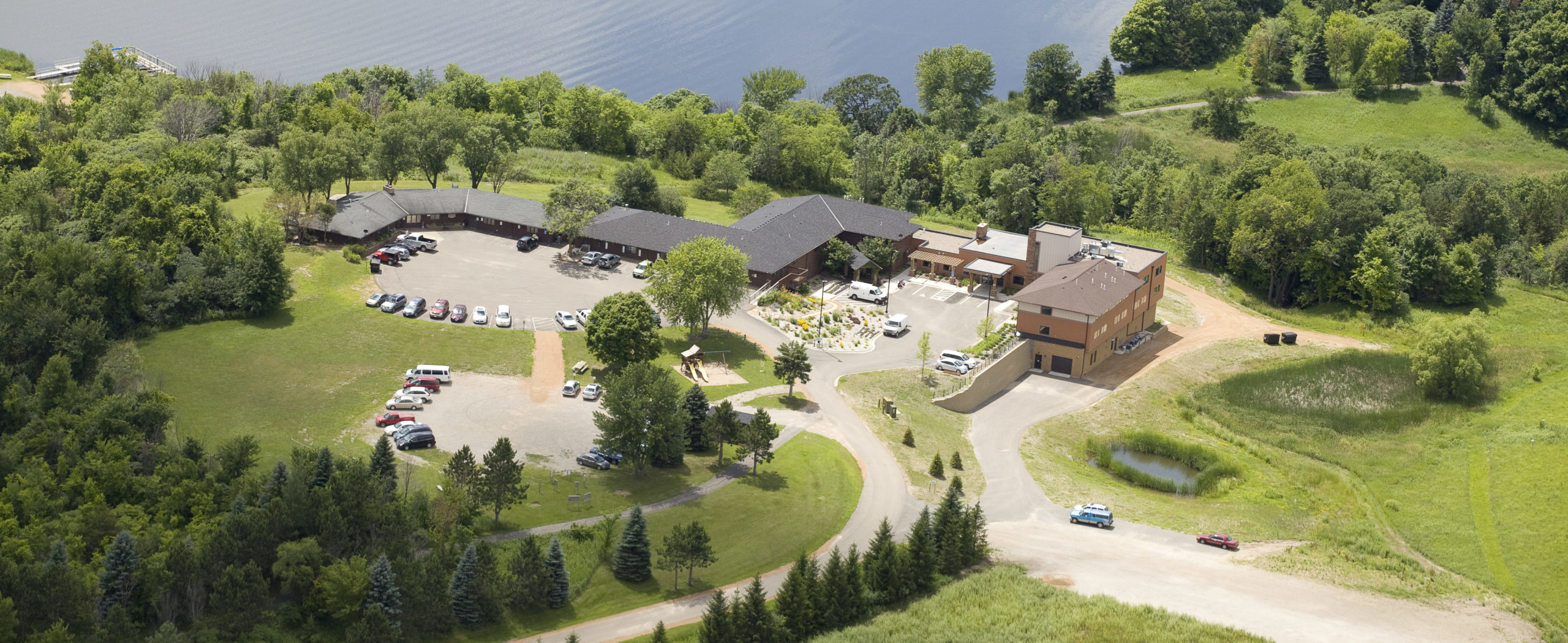 Green campus with buildings by a lake, seen from above