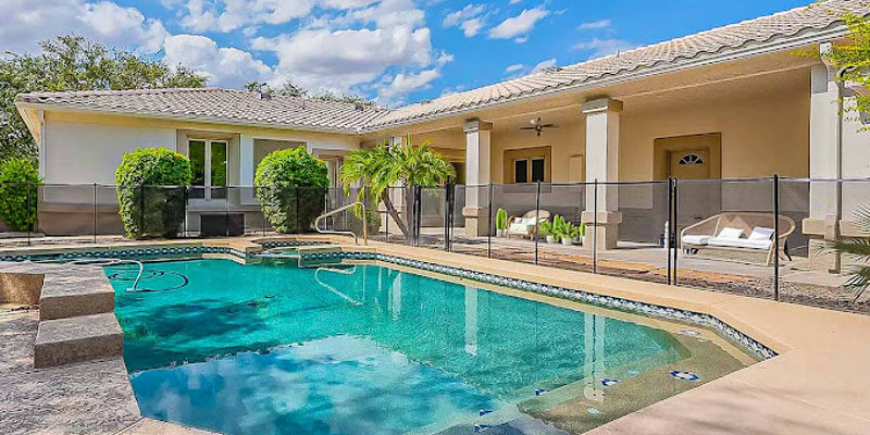  A sunlit backyard with a sparkling pool, surrounded by greenery and a spacious patio, offering a relaxing and private outdoor retreat.