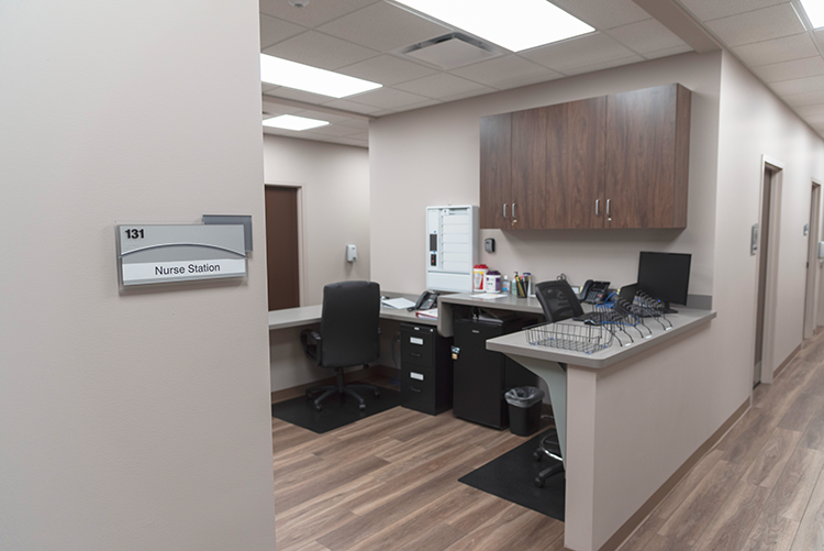 BrightView Health nurse station with work counters, computers, office chairs, overhead wood cabinets, and wood-look flooring