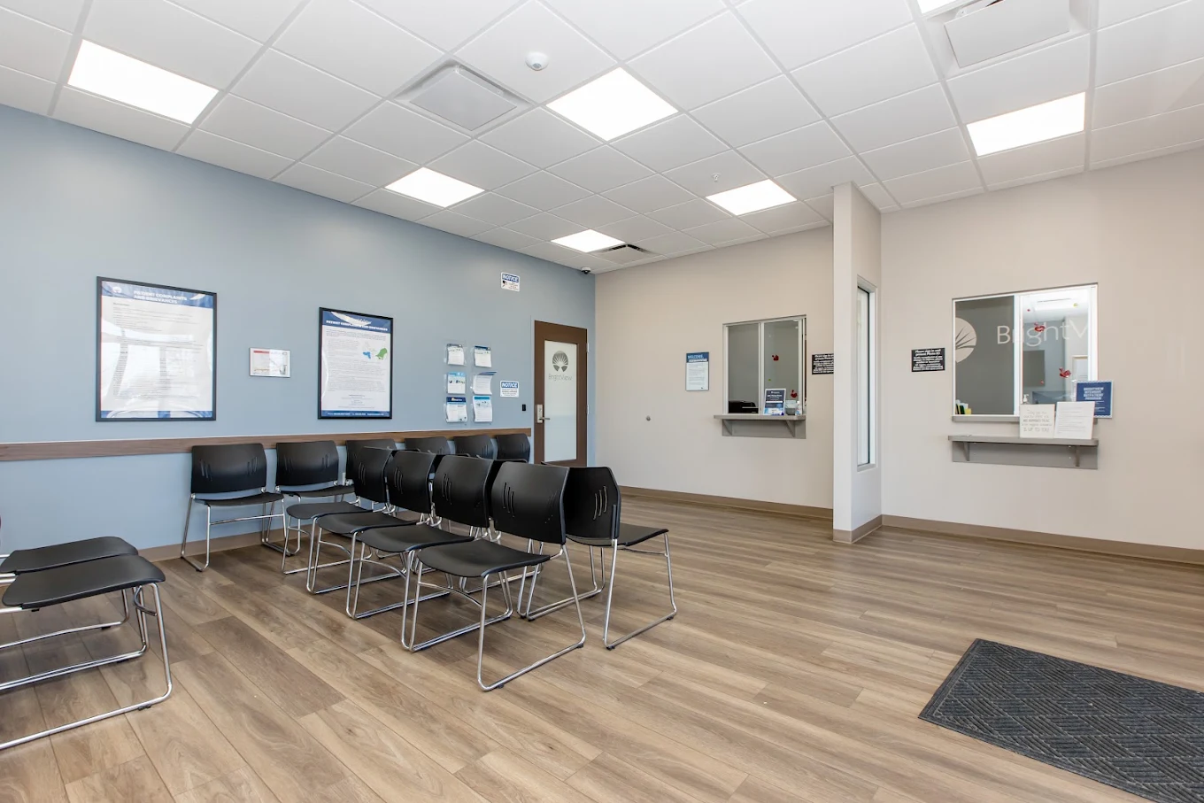 Spacious patient waiting area with rows of black chairs and check-in service windows
