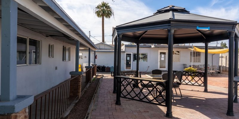 A spacious outdoor patio featuring a shaded gazebo, perfect for relaxation and gatherings, under a bright sky with a palm tree nearby.