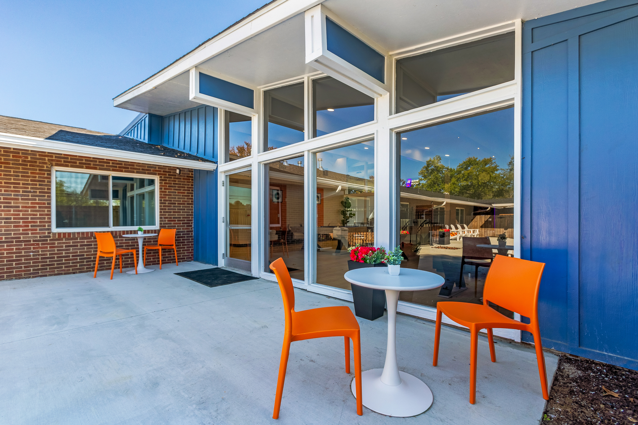 Patio with orange chairs beside blue siding and tall windows