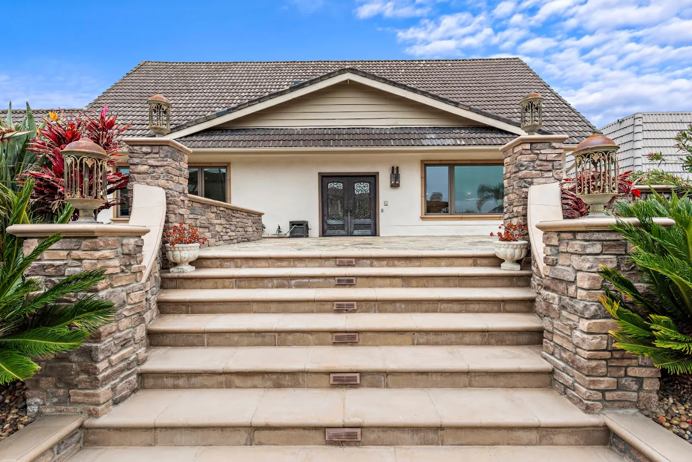Front entrance with stone columns, wide steps, tropical landscaping, and decorative doors